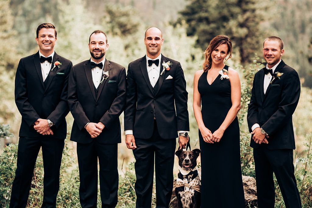 Wedding party lined up outdoors with dog in formal attire.
