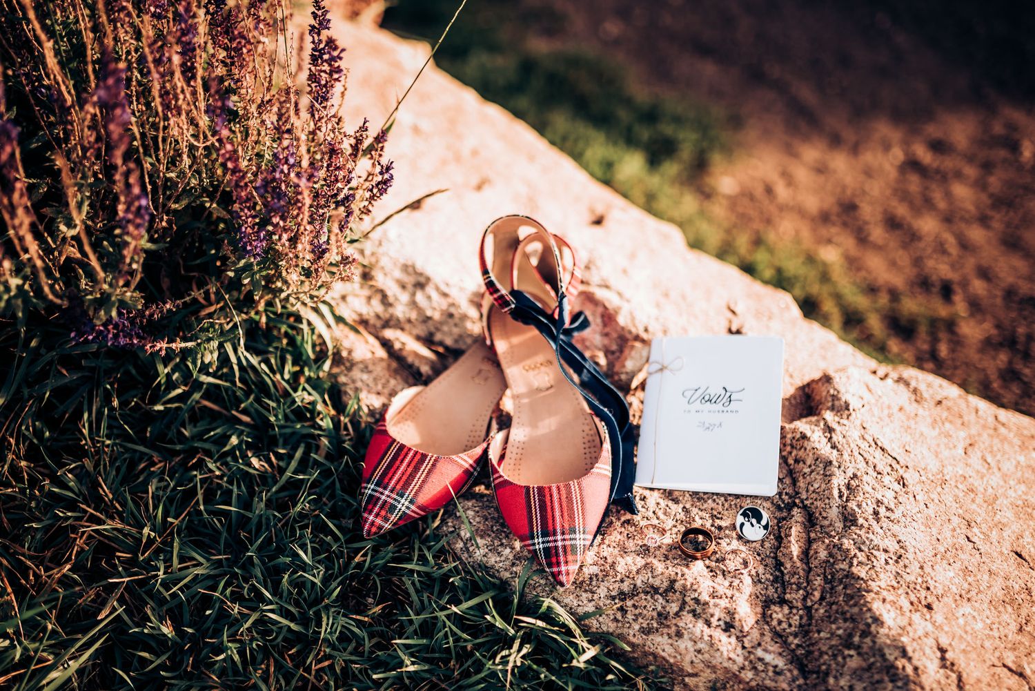 Red plaid flats and wedding stationery arranged artistically on stone.