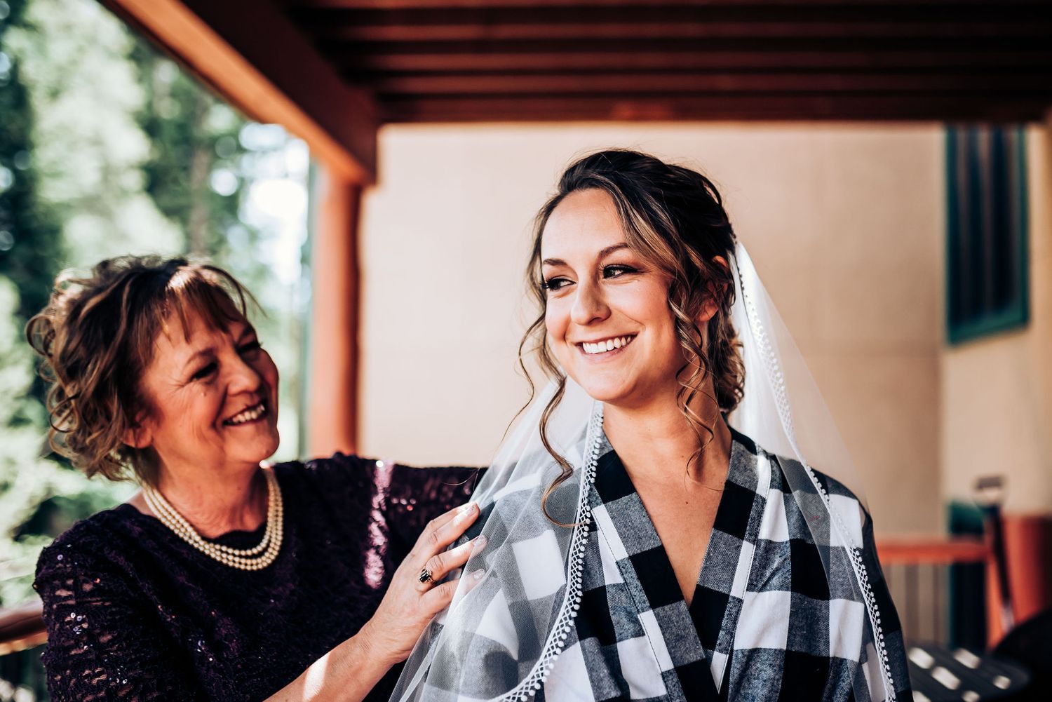 Getting ready scene with bride wearing plaid robe while someone helps style her hair.