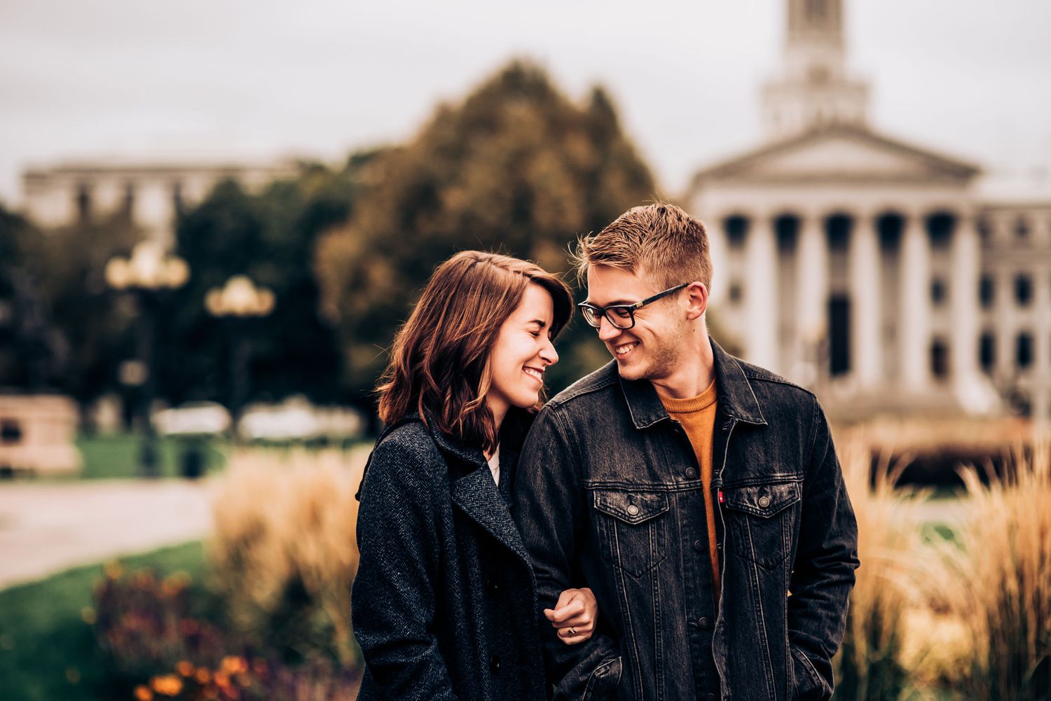 A couple stands together in front of a stately government building on an autumn day.