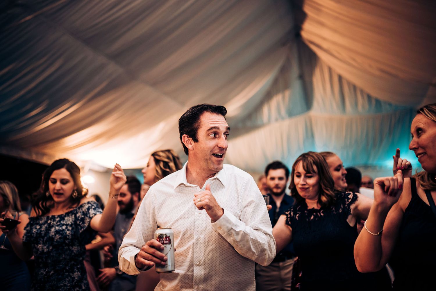 Energetic guest dancing and celebrating at a wedding reception under draped tent ceiling.