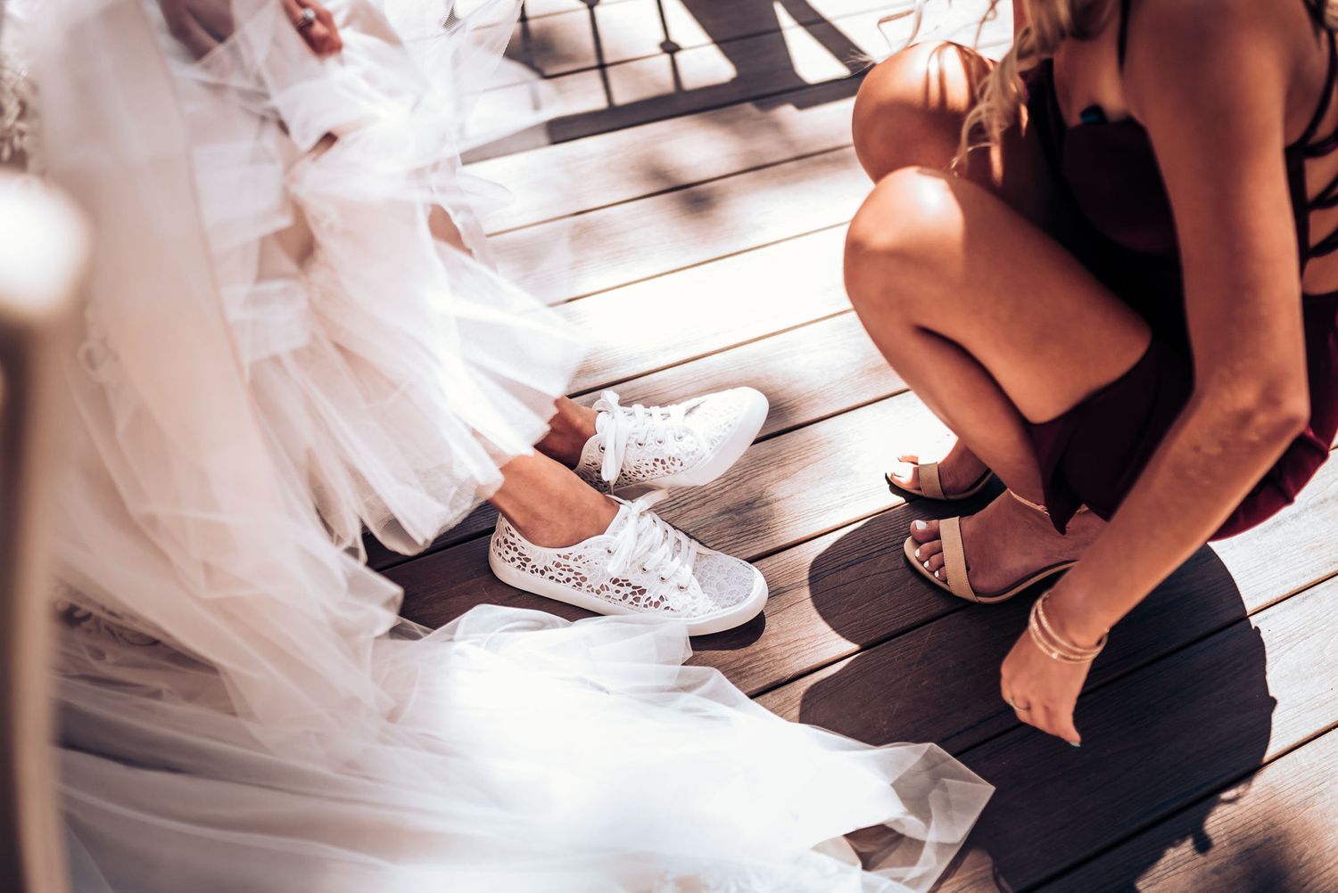 Close-up of white sneakers being put on under a flowing wedding dress.