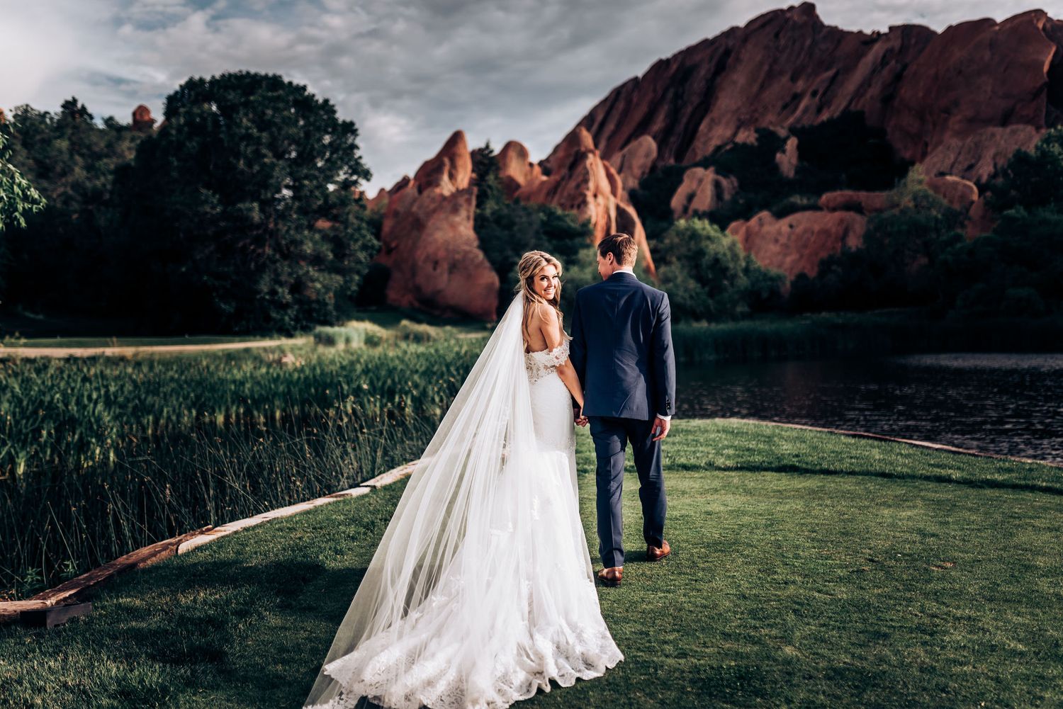 Wedding couple walking on grass path with stunning red rock formations at Garden of the Gods.