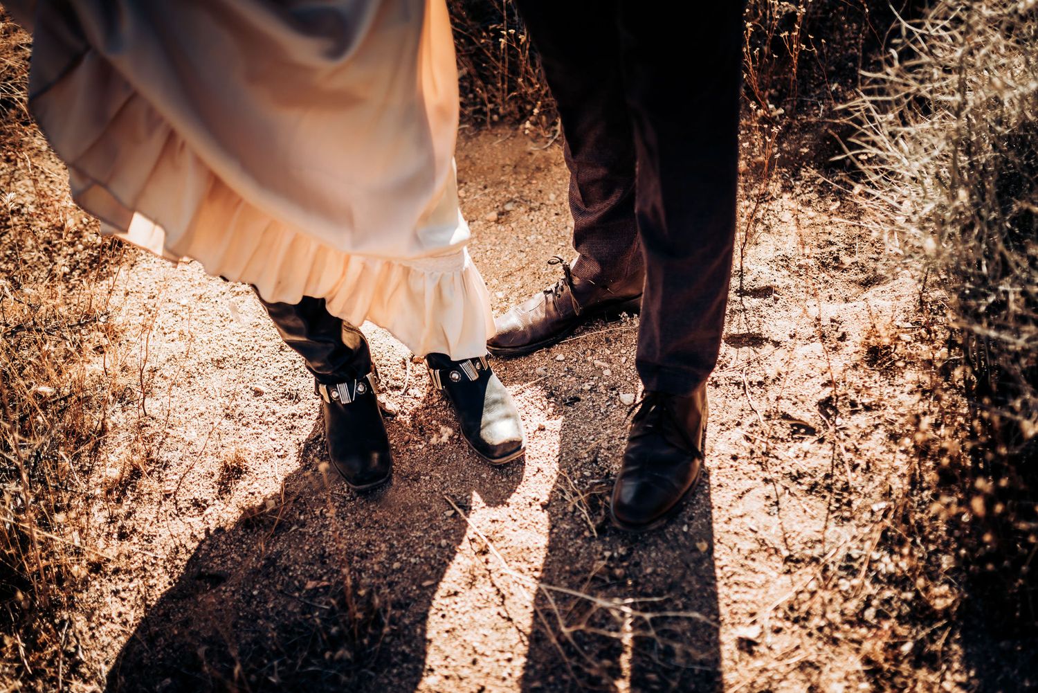 Two pairs of boots stand close together on a sunlit path with fallen leaves.