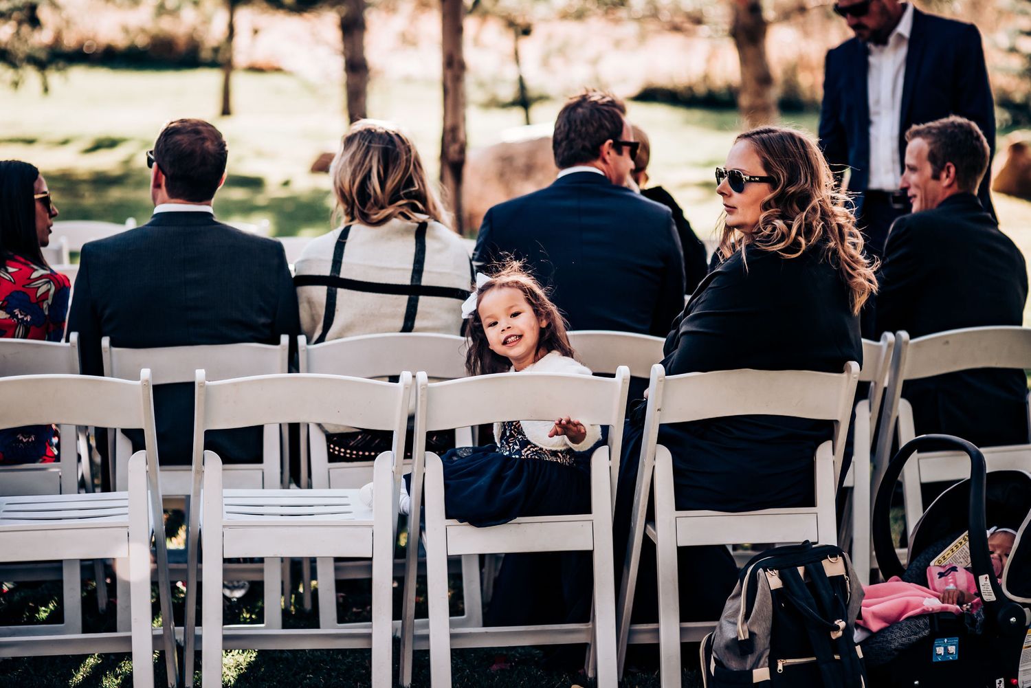 Wedding guests seated in white chairs at an outdoor ceremony venue.