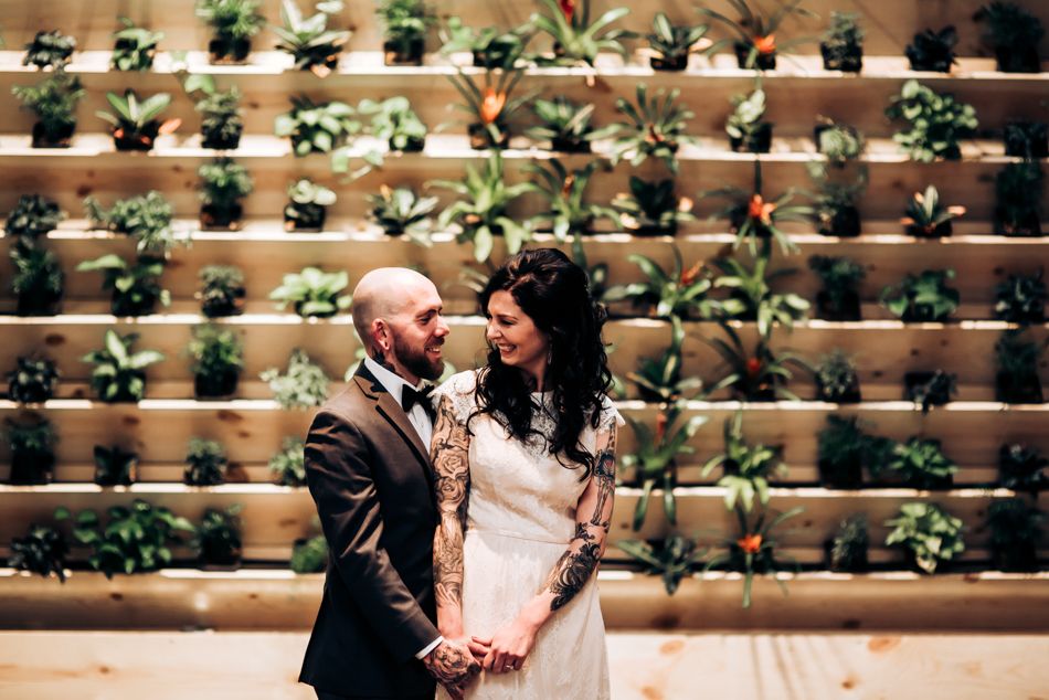 Romantic wedding portrait against decorative wall with potted plants.
