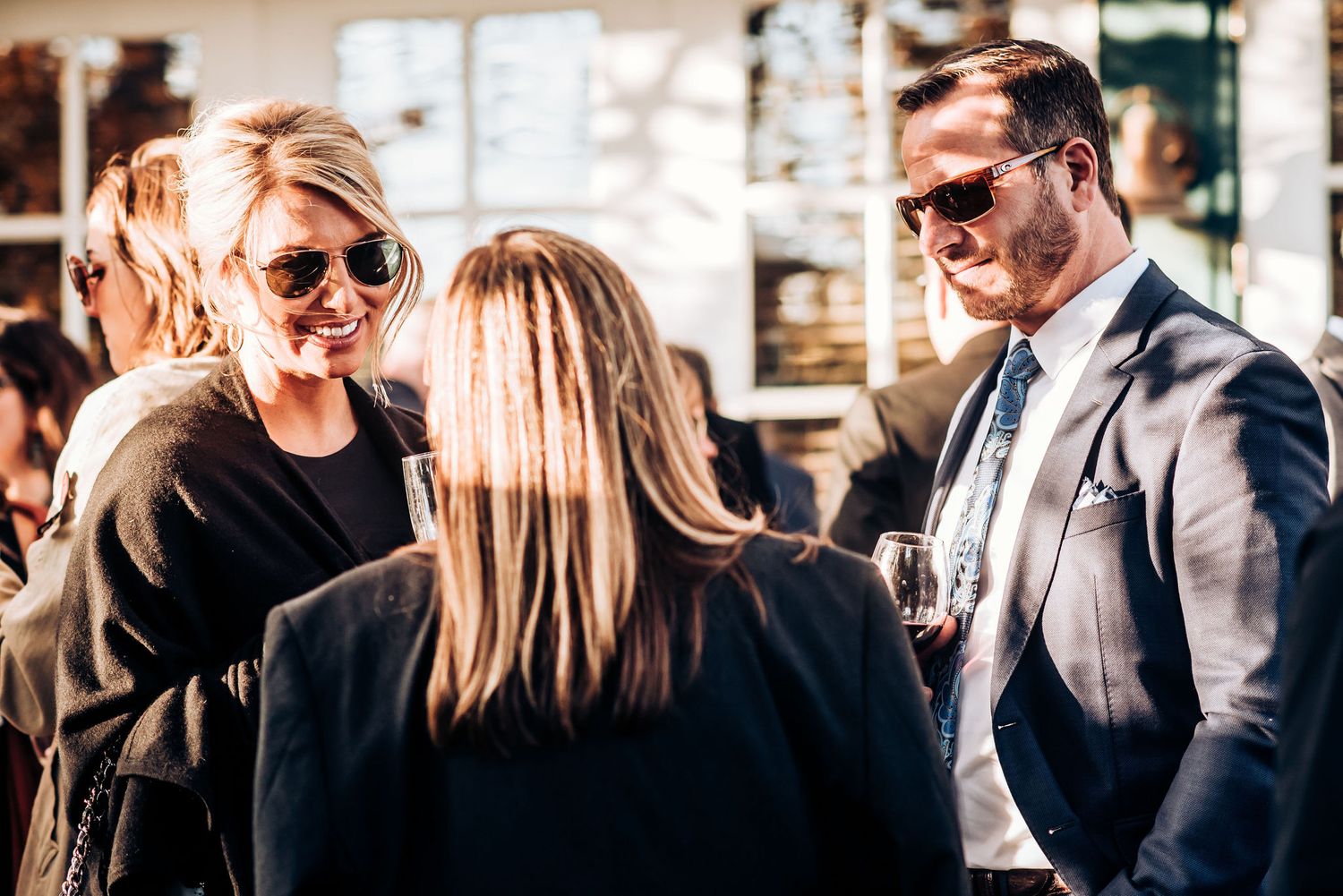 Three people engaged in casual conversation at an outdoor gathering with natural lighting.