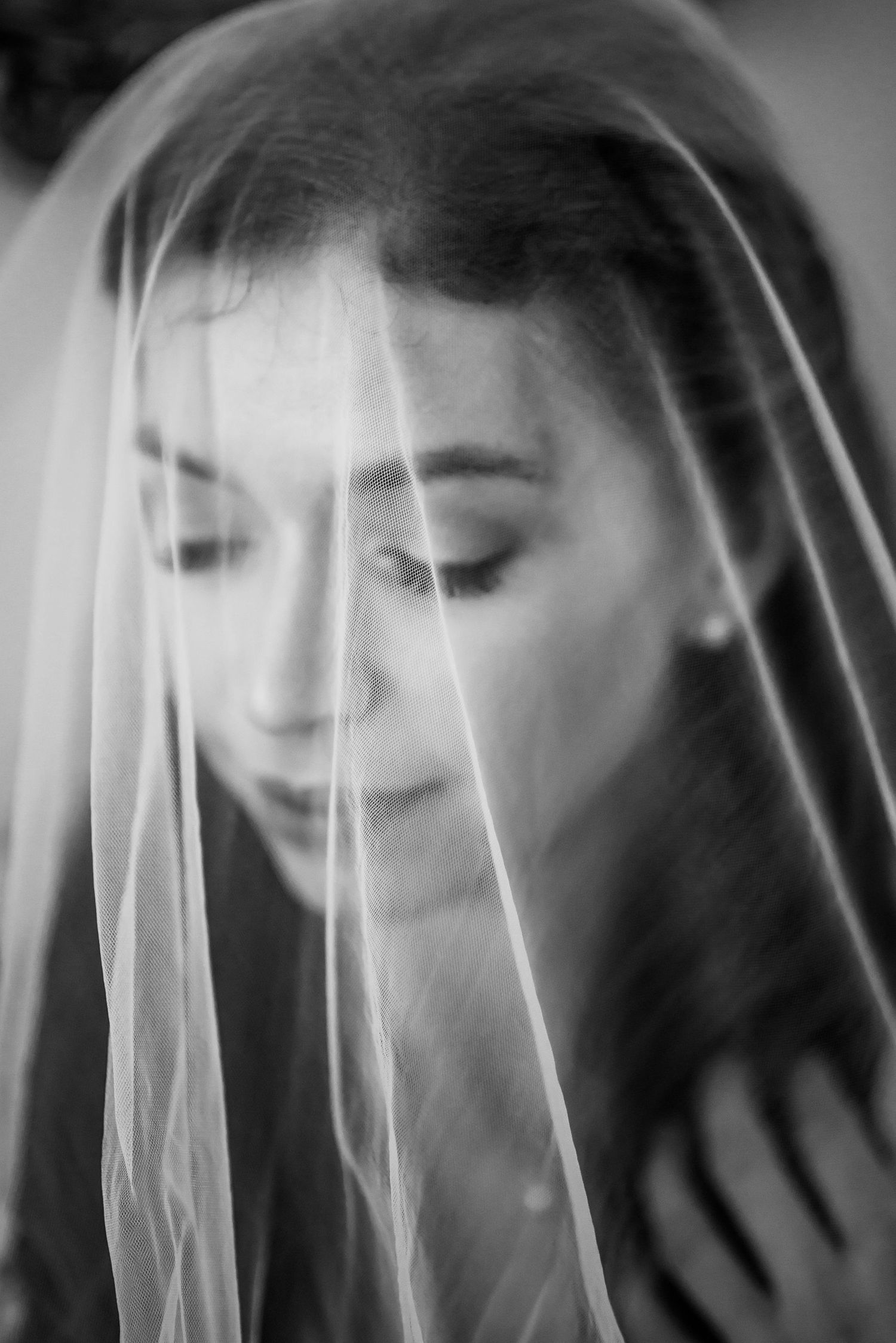 Artistic black and white portrait showing a soft veil draping over a downward tilted face.