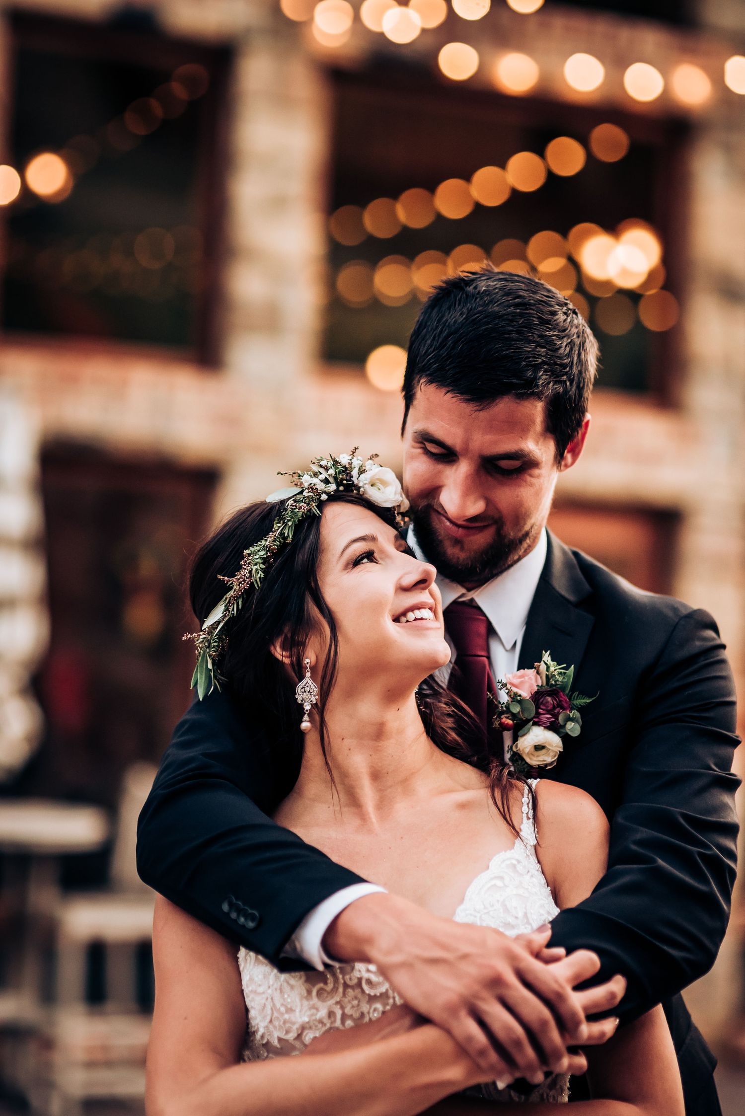 Joyful candid moment between newlyweds laughing together under twinkling lights at their reception.