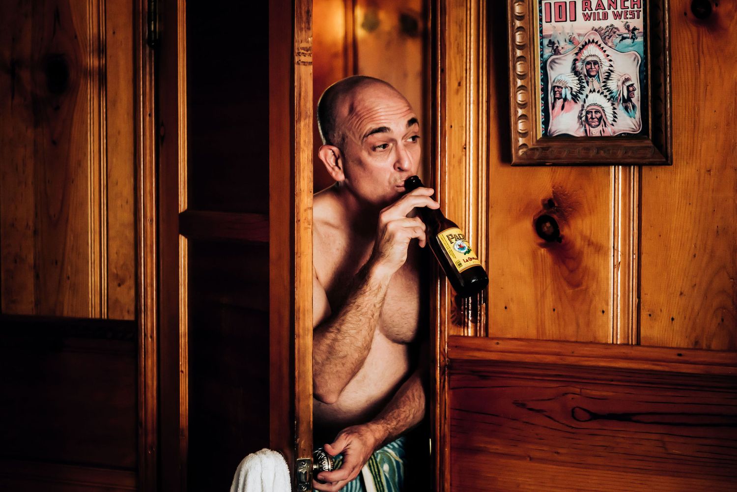 Person drinking from a bottle in a dark wooden paneled room with vintage decor.