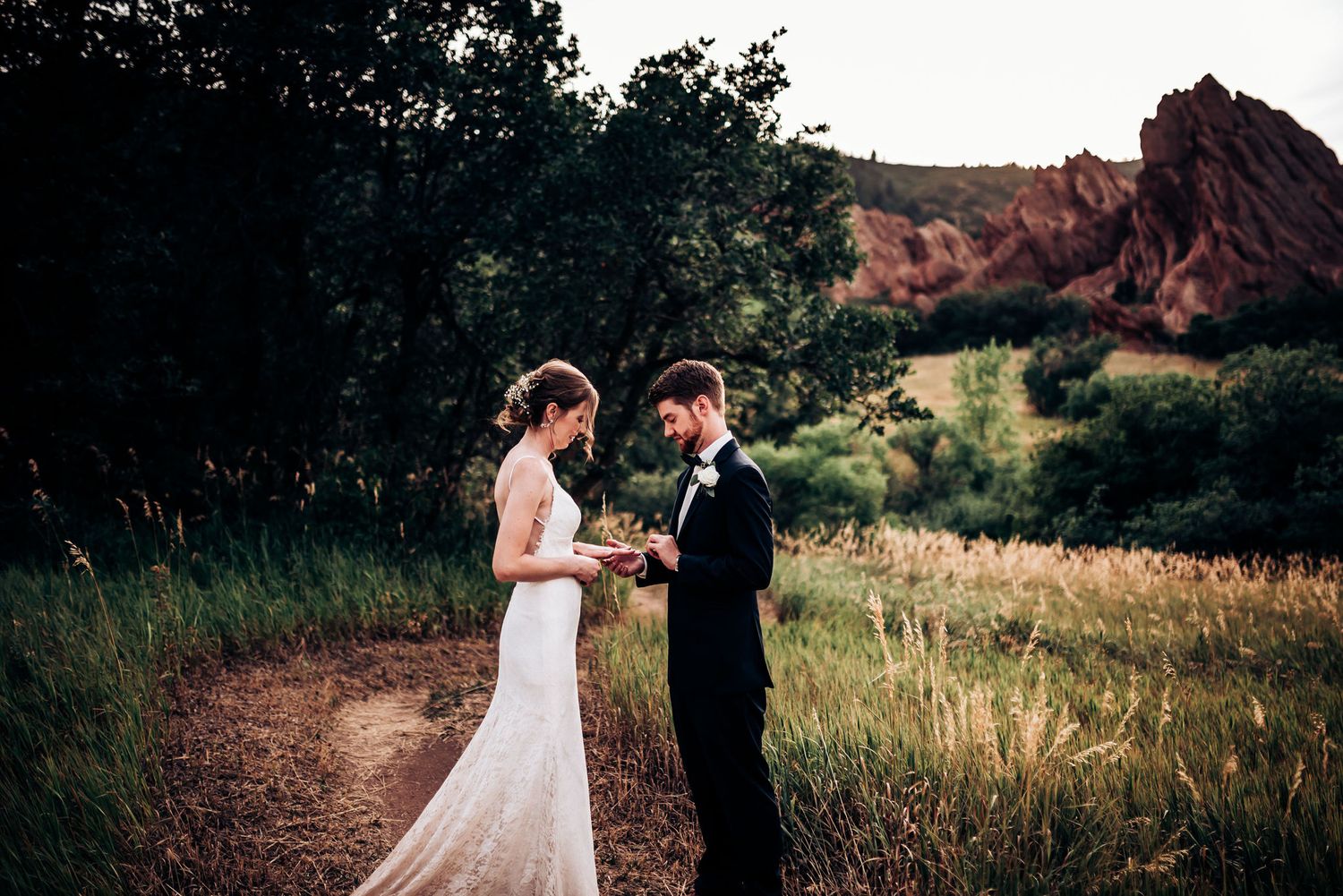 Couple exchanges vows in natural setting with red rock formations in background.