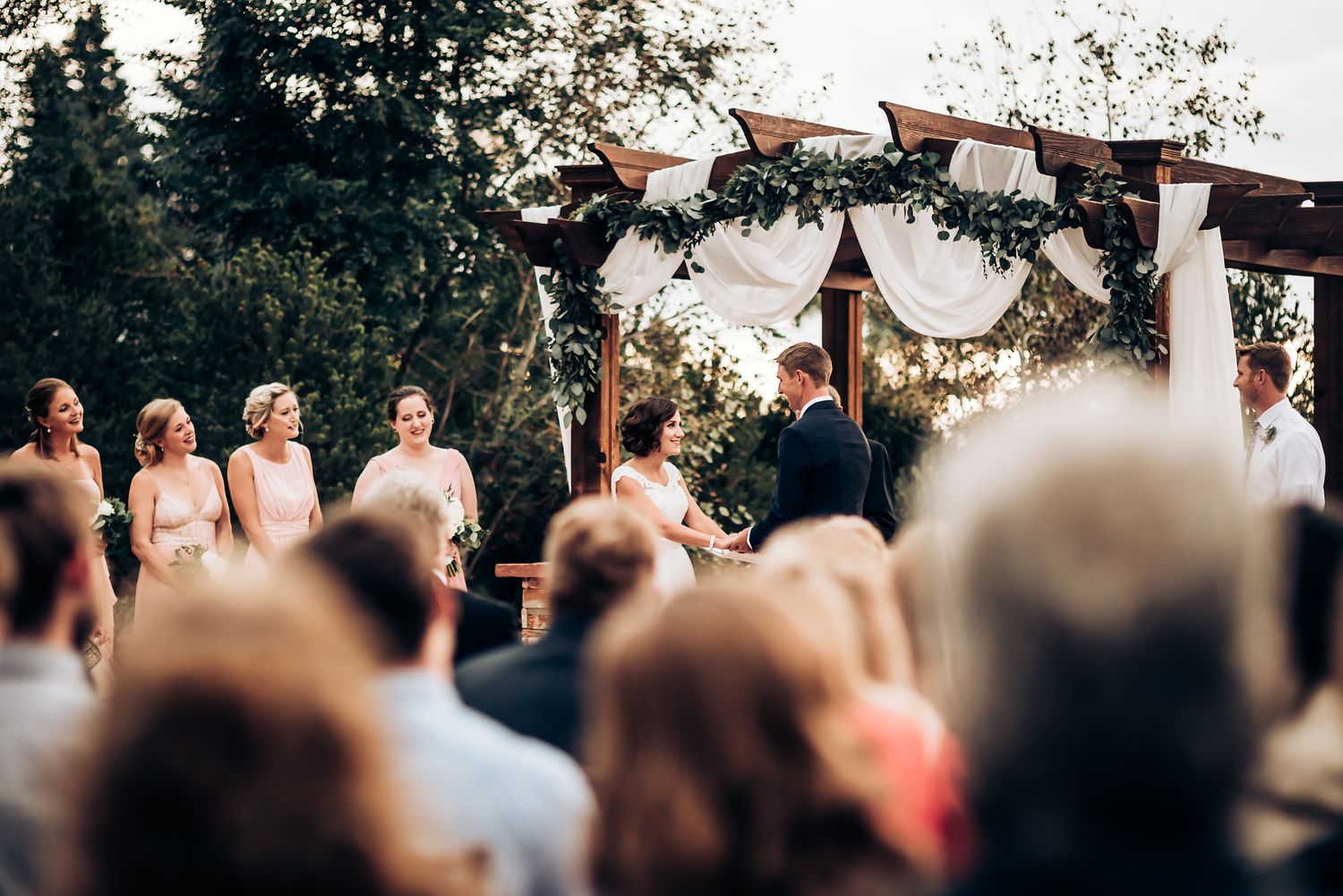 Wedding ceremony view from behind guests with decorated arch and mountain backdrop.