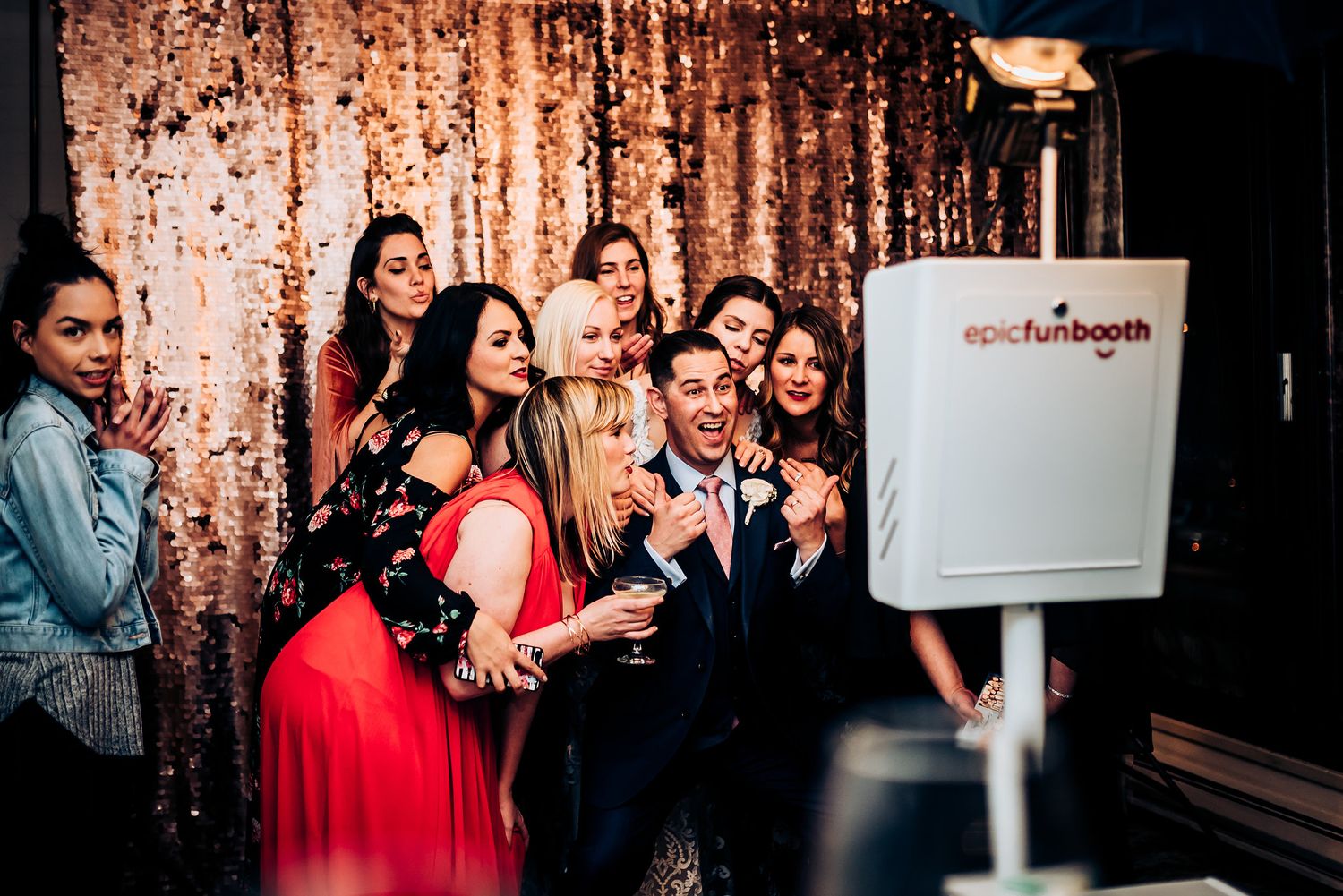 Party guests pose together in front of a sparkly rose gold sequin backdrop.