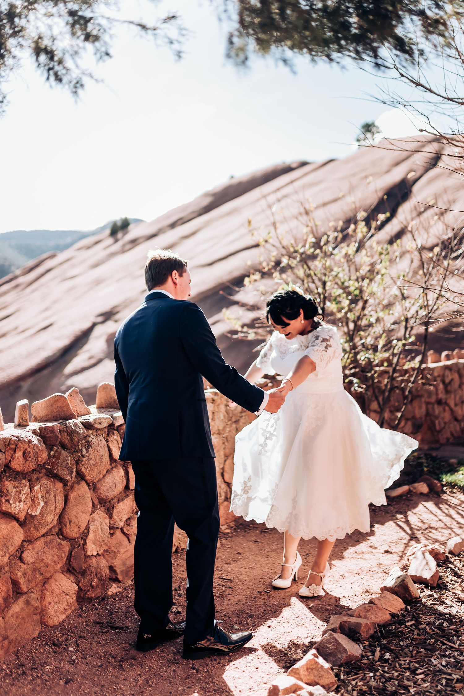 Wedding couple walks down stone steps with desert landscape in background.