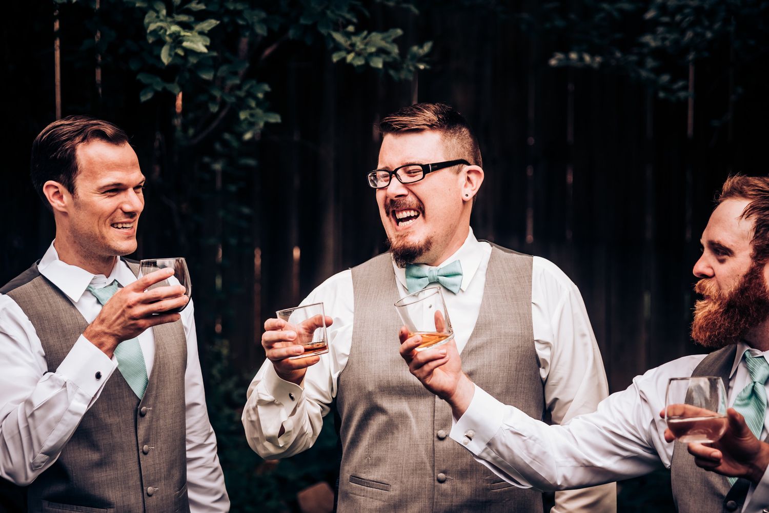 Groomsmen in matching vests share laughter and drinks during wedding celebrations.