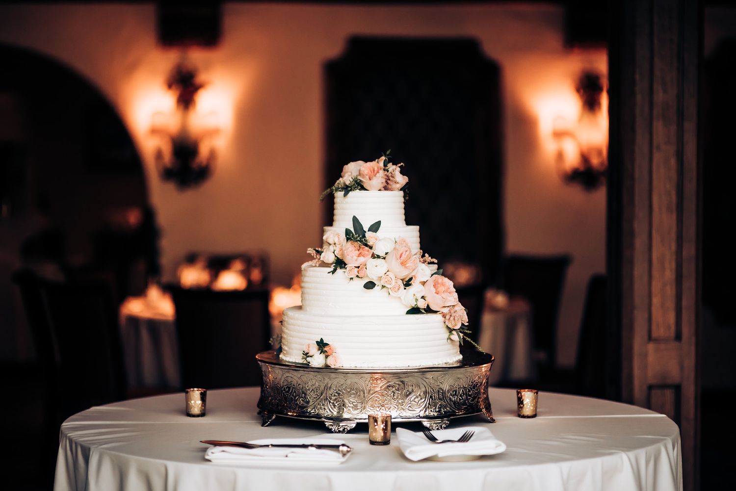 Elegant white wedding cake decorated with pink florals displayed on round table.