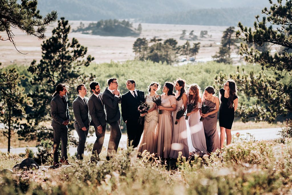 Wedding party poses for photos on a mountainside overlooking a scenic valley landscape.