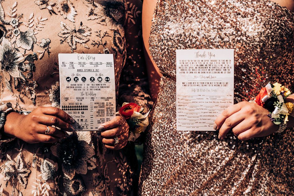 Hands hold up wedding invitations against patterned and sequined fabric backgrounds.