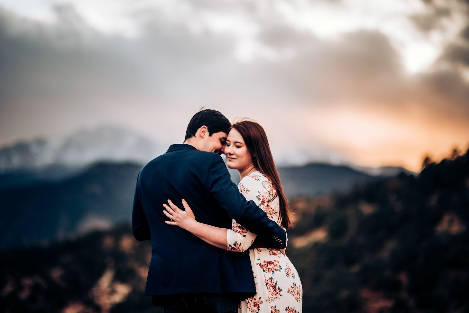 Romantic couple embraces against a dramatic mountain sunset backdrop in a stunning outdoor engagement photo.