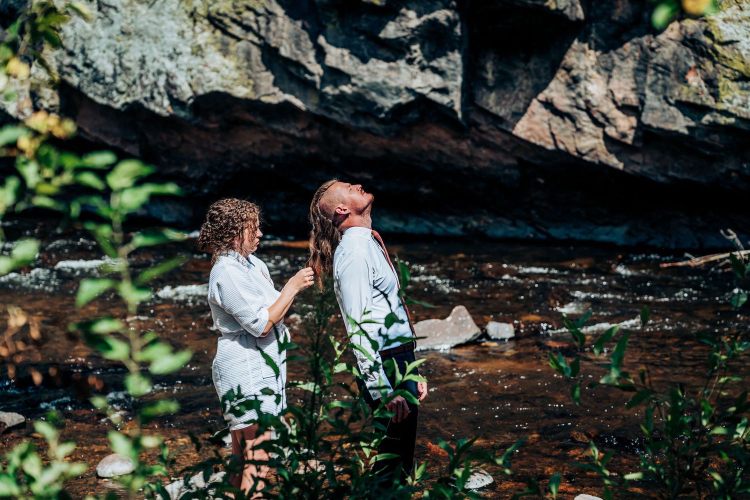 Two people in white outfits standing by rocky outcrop near water.