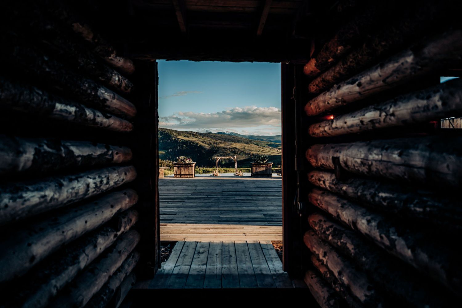 View through wooden cabin window frame of mountain landscape and deck.