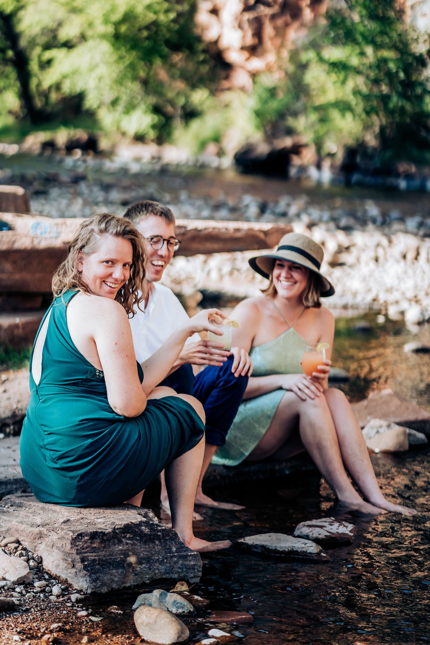 Friends relaxing together by a creek on rocky shore during summer day.