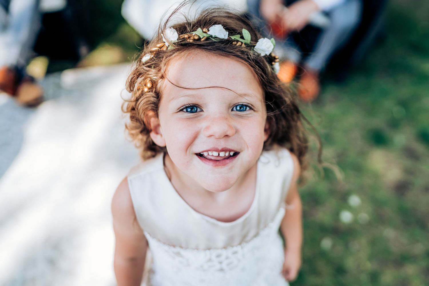A young attendee wearing a white dress and floral crown at an outdoor event.