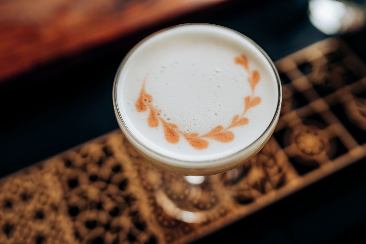 Elegant cocktail with frothy white top and decorative orange leaf pattern in stemmed glass.