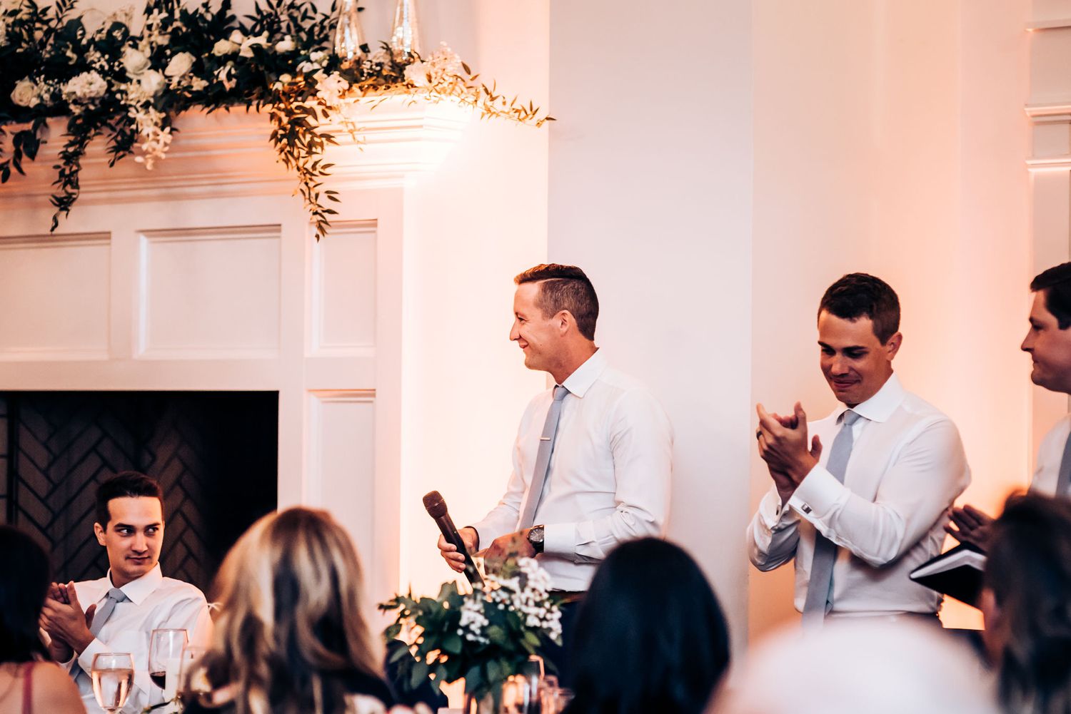 Wedding reception speech in progress at elegantly decorated venue with fireplace.