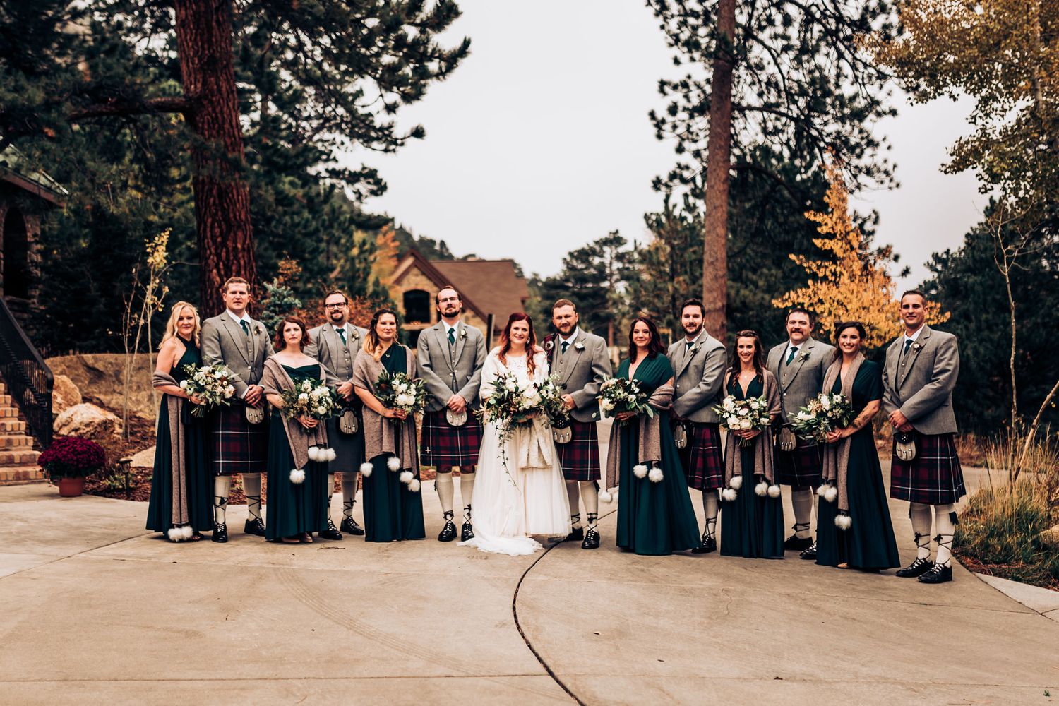 Wedding party in traditional Scottish kilts poses for formal group photo outdoors.