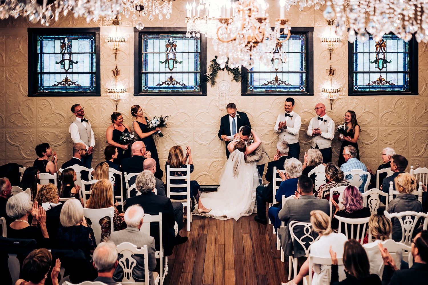 Wedding venue decorated with crystal chandeliers and stained glass windows during ceremony.