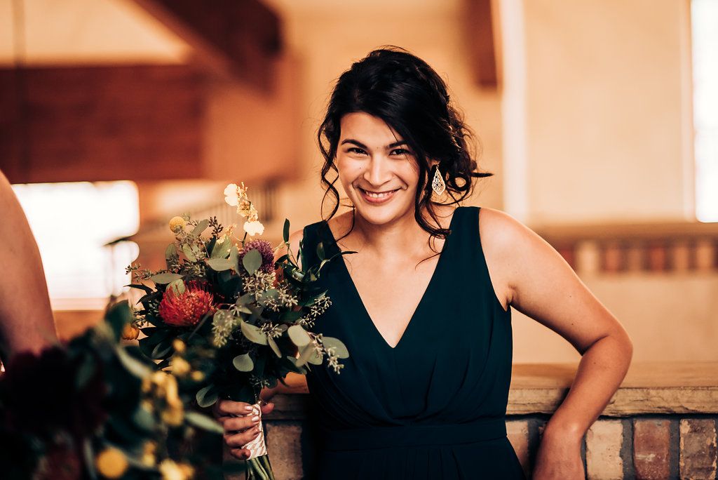 Bridesmaid in navy dress holding floral bouquet at indoor venue.