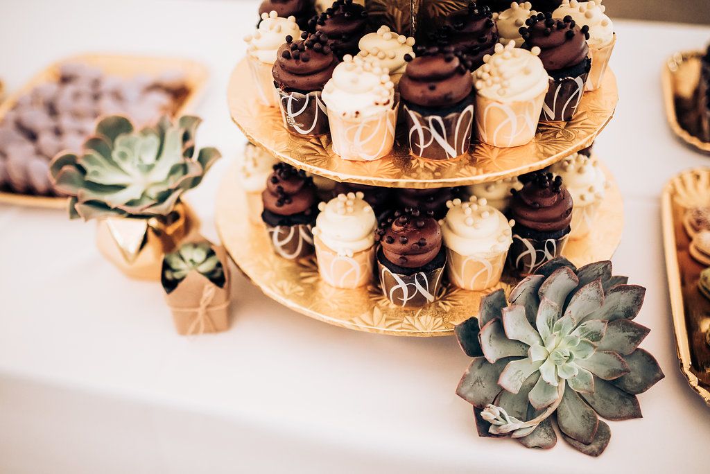 Close-up of chocolate and vanilla cupcakes on gold tiered stand with succulent decorations.