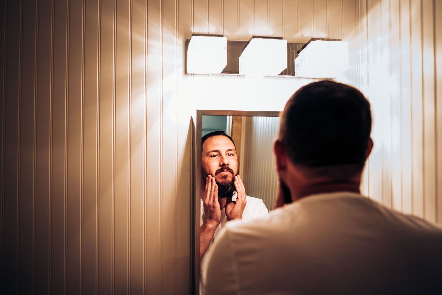 Person in white shirt adjusting tie while looking in bathroom mirror.