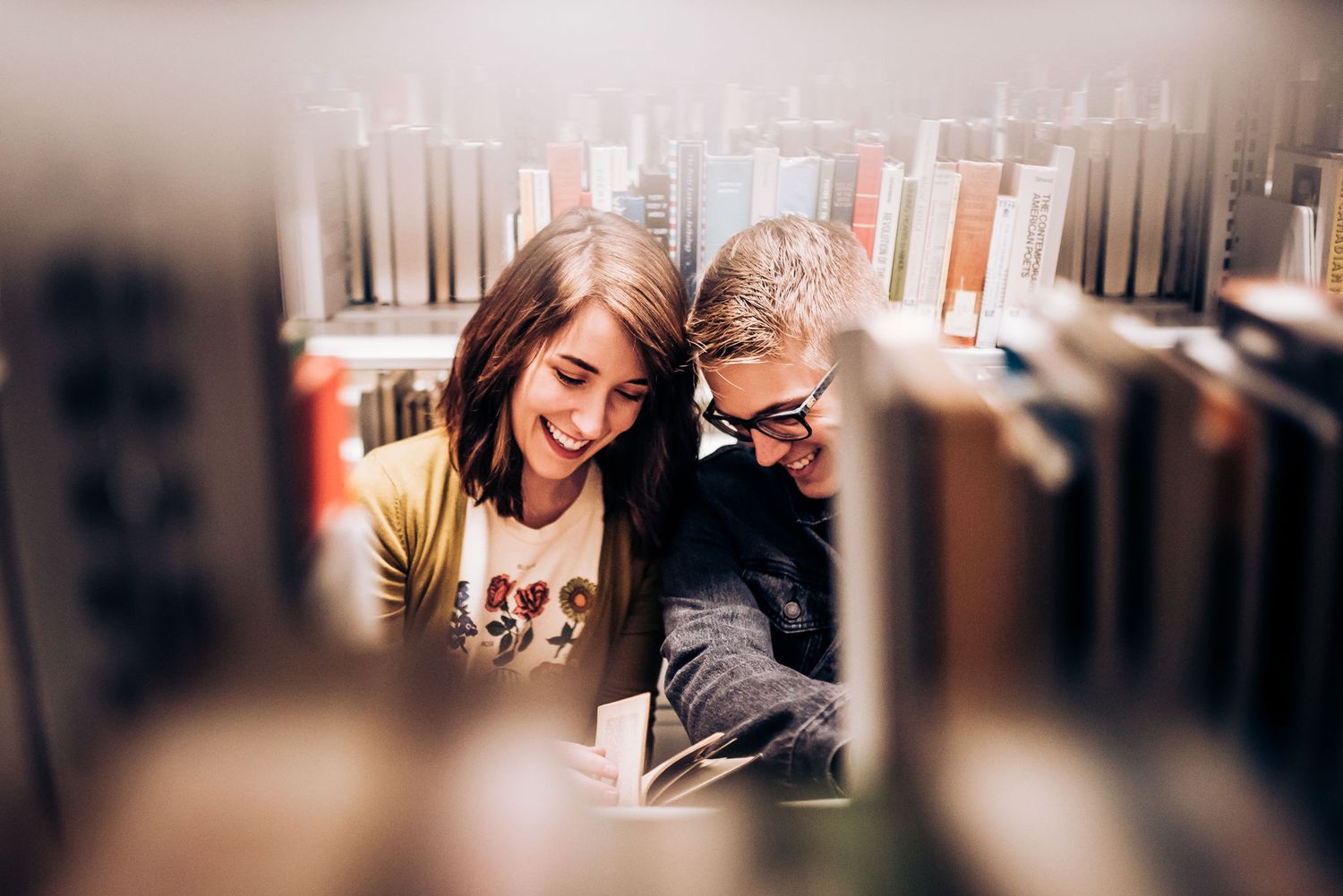 A couple shares an intimate moment between library bookshelves.