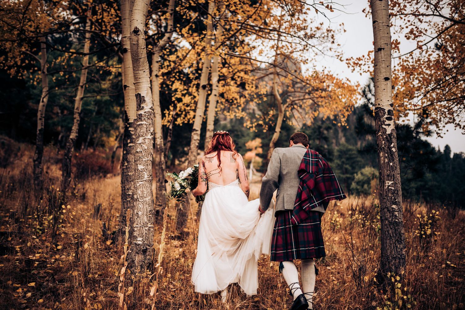 Wedding couple walking through autumn aspen grove in Scottish attire.