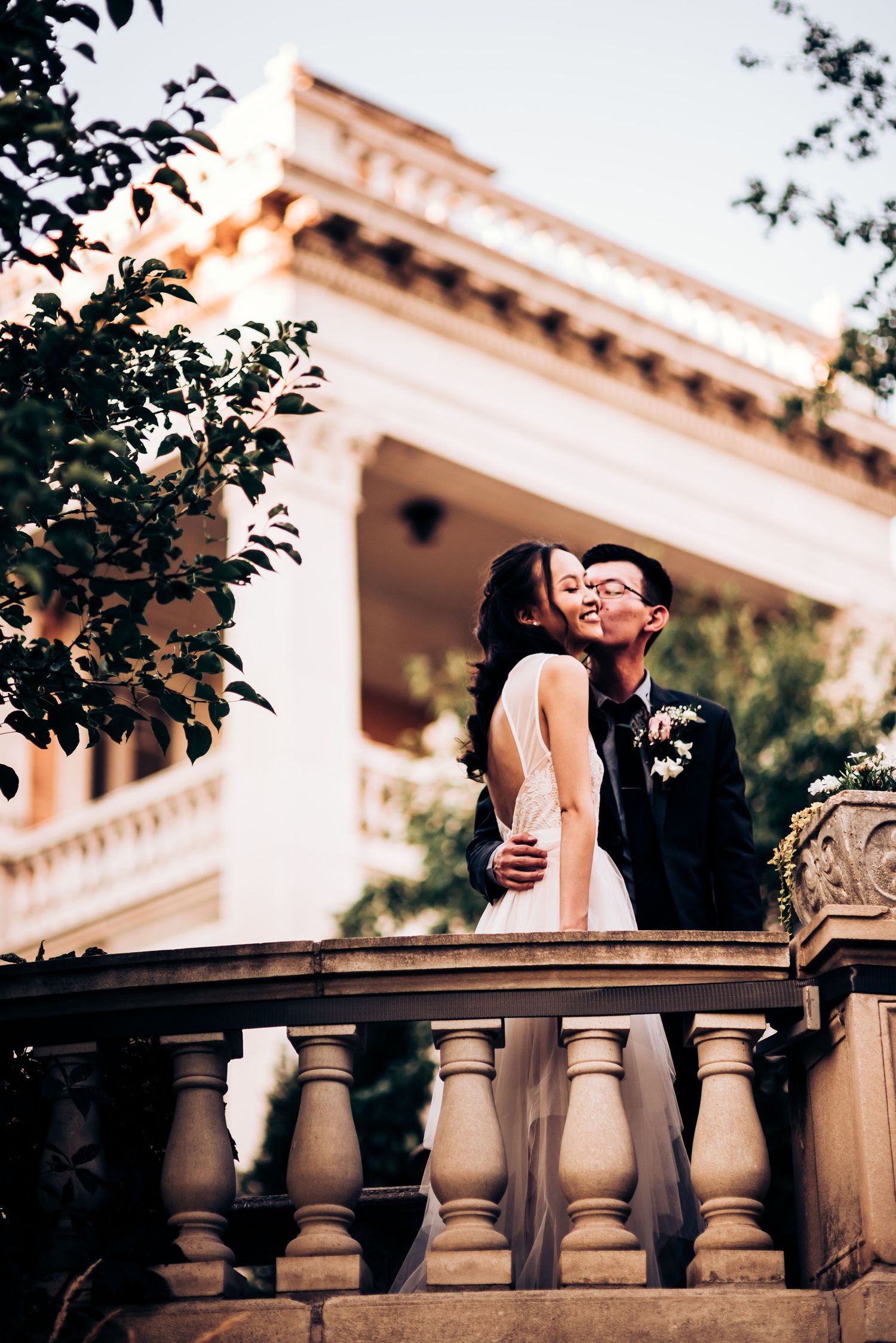 A couple shares a tender moment on a classic stone balcony with architectural details.