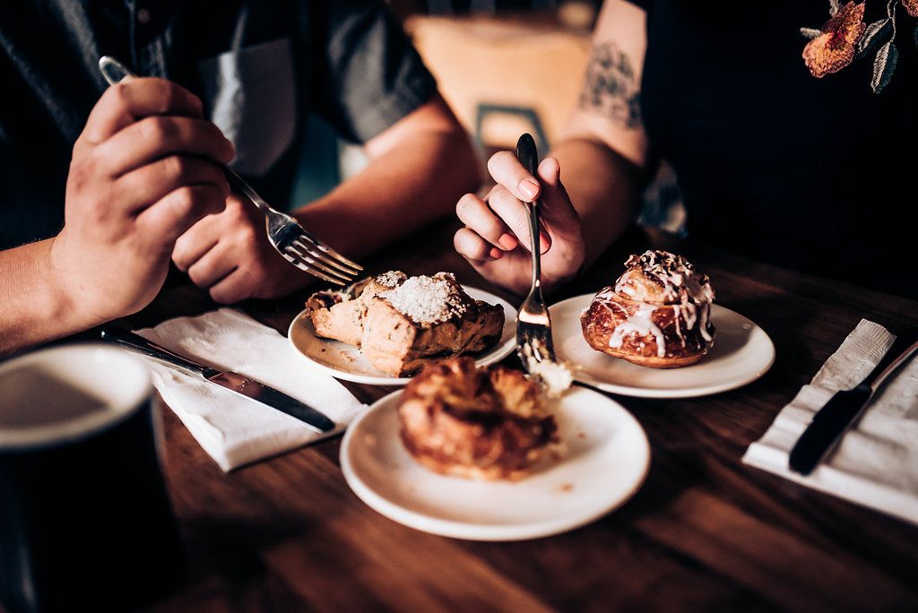 Close-up shot of hands using forks to eat decadent desserts on white plates.