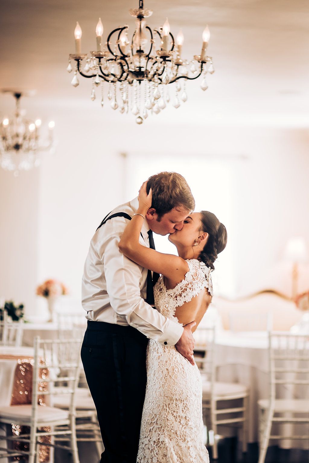 A romantic first dance moment under elegant crystal chandeliers in a white ballroom.
