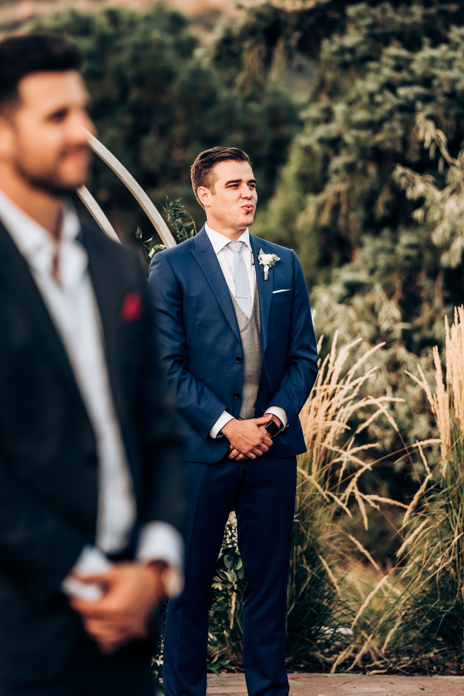 Groomsmen in navy suits standing at attention during outdoor wedding ceremony.