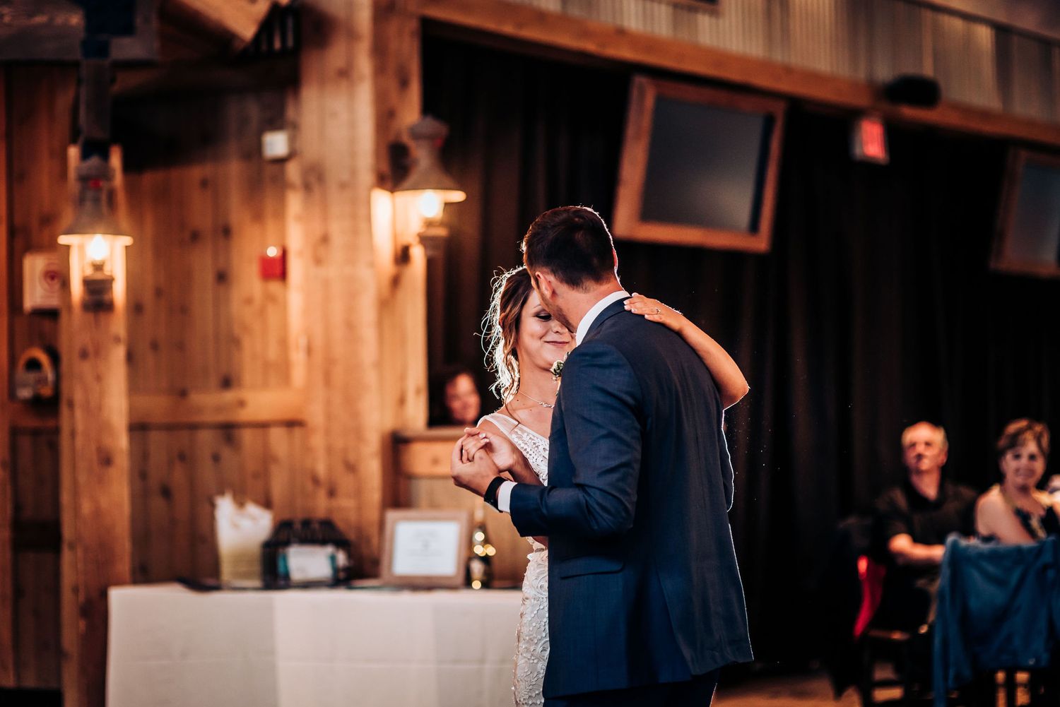 Intimate dance moment in rustic reception hall with warm ambient lighting.