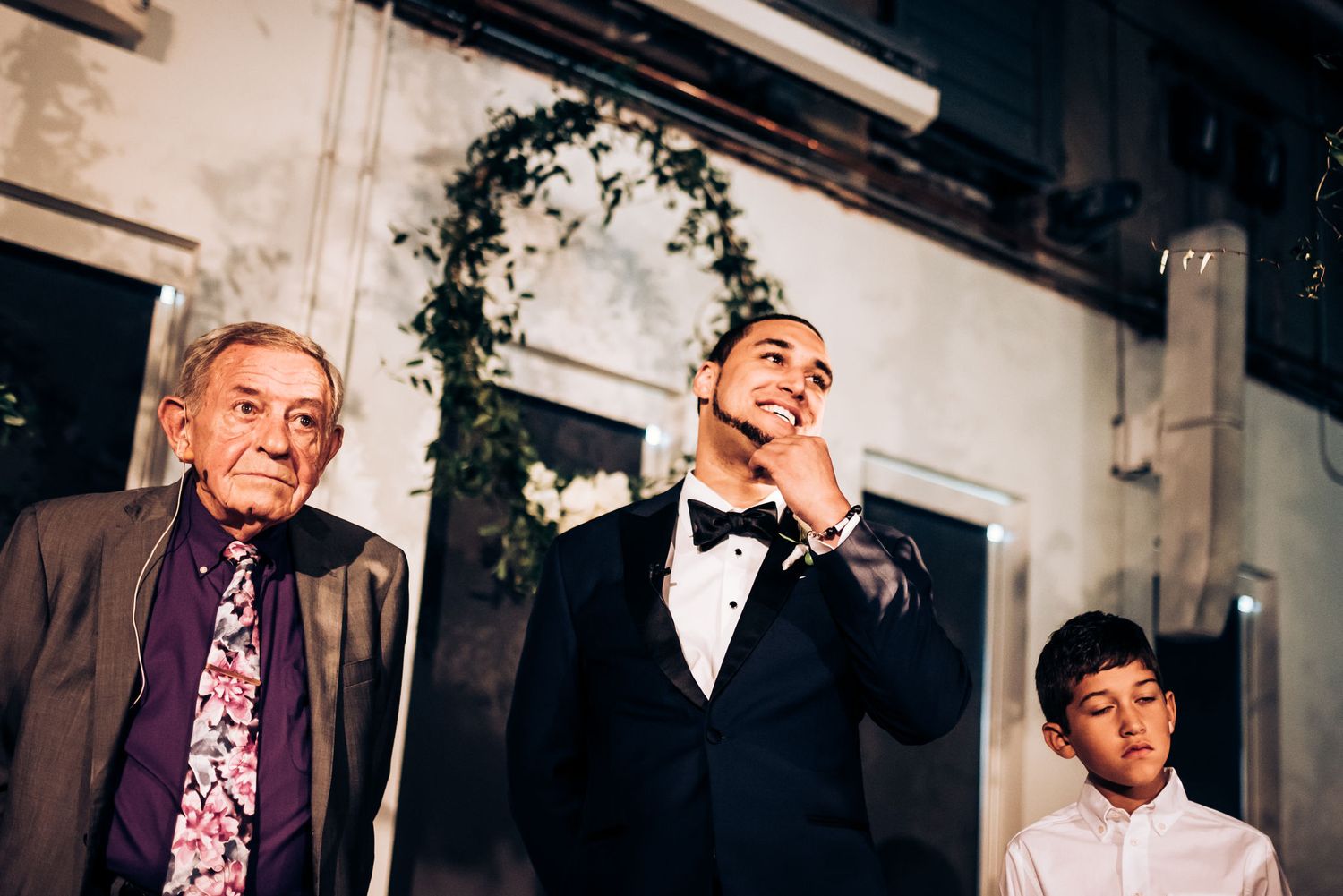Wedding attendees exude joy during an emotional speech under a floral archway.