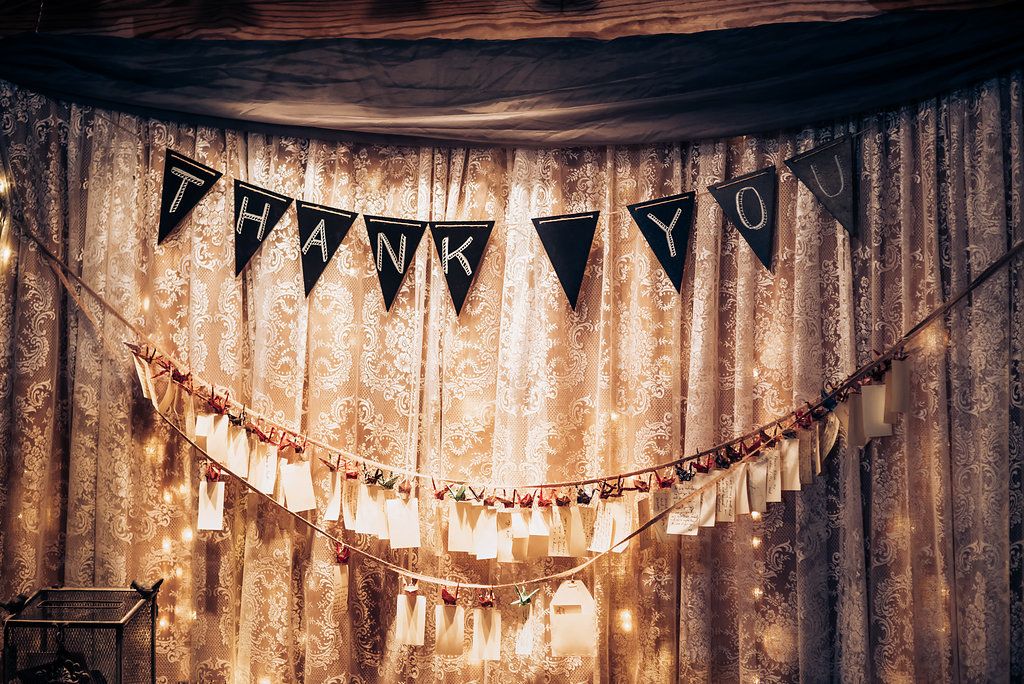 Vintage-style wedding decorations with hanging string lights and pennant banners against a textured backdrop.