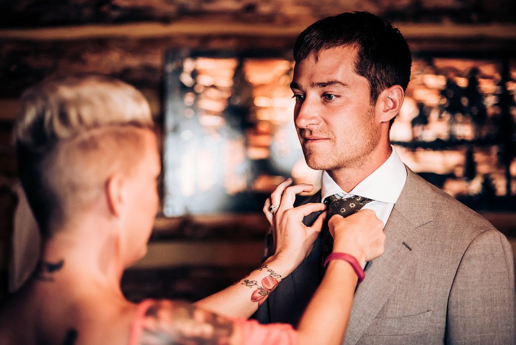 A bow tie is being adjusted on a man wearing a light grey suit.
