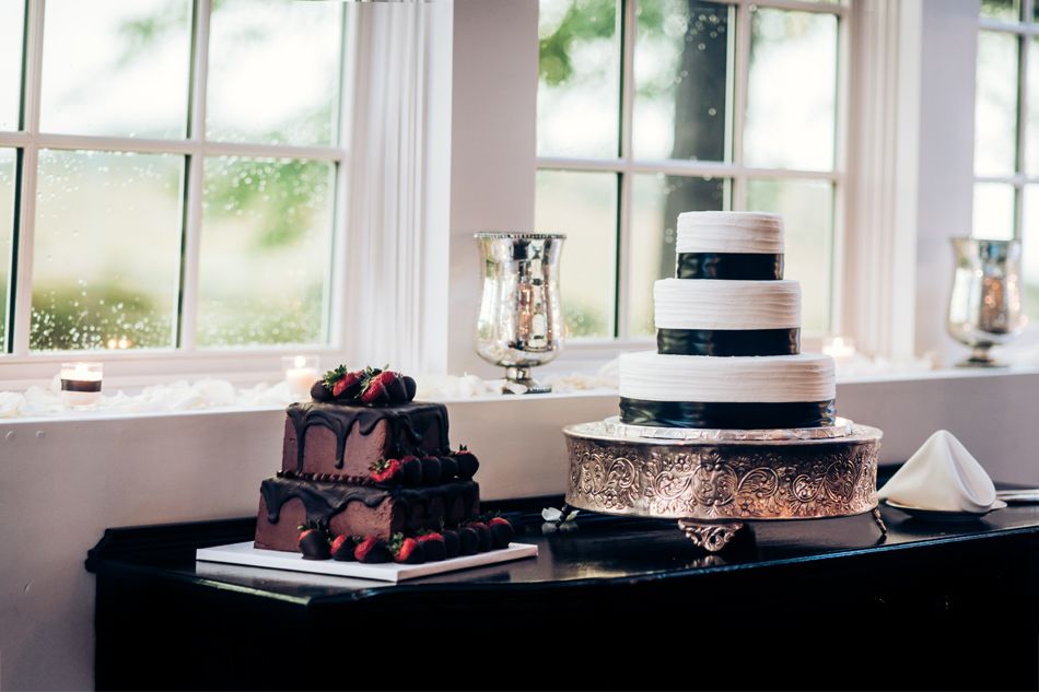 Elegant black and white tiered wedding cake displayed on table near window with smaller square cake alongside.