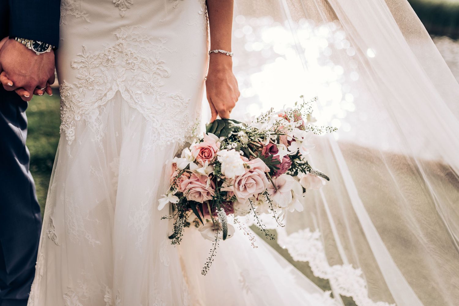Close-up of bridal bouquet with pink roses and flowing white dress train.