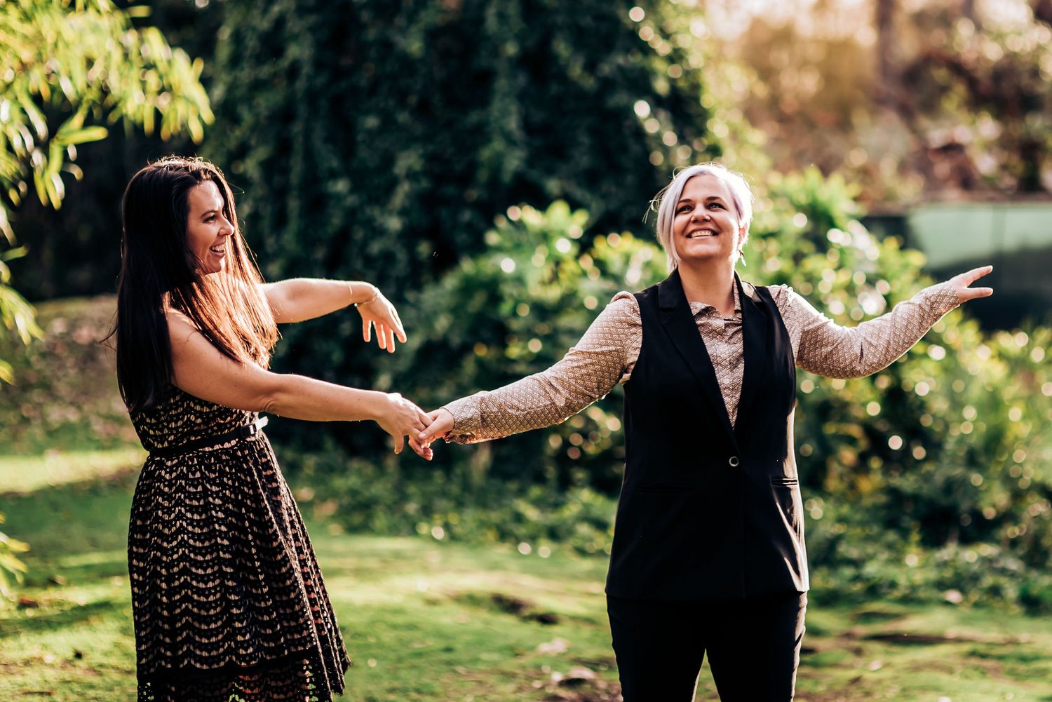 Two people dance joyfully in a sunlit garden setting.