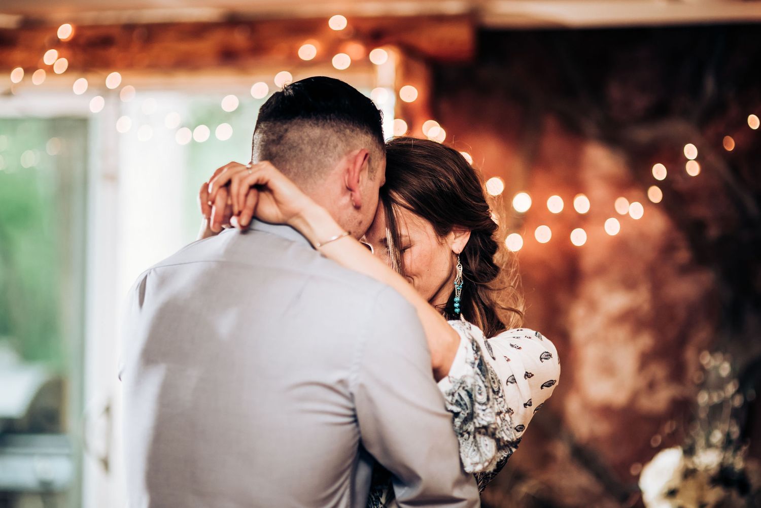 Romantic couple dancing close together under glowing string lights at an evening reception.