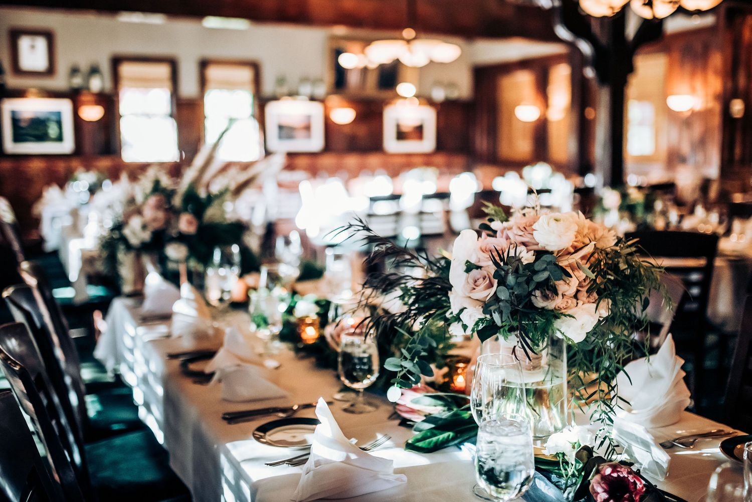 Wedding reception venue with elegant table settings and floral centerpieces in warm lighting.