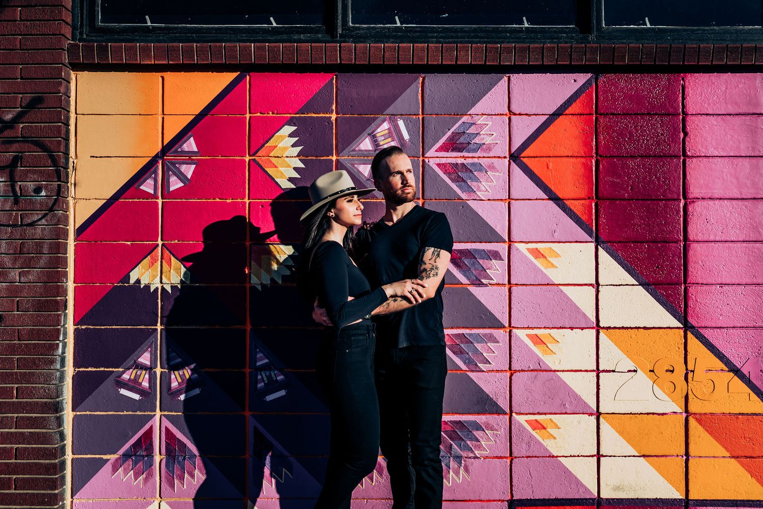Couple poses against geometric wall mural featuring orange and pink patterns.
